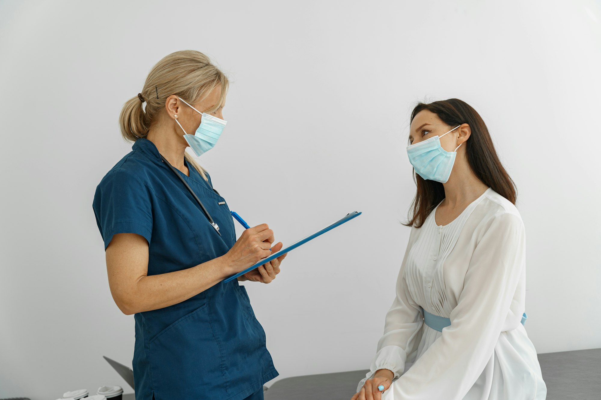 Doctor wearing protection mask against covid taking notes during consultation with patient